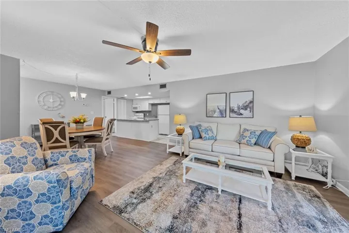 Living room with ceiling fan with notable chandelier, a textured ceiling, and dark hardwood / wood-style flooring