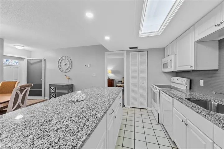 Kitchen featuring white appliances, light stone countertops, sink, white cabinets, and a skylight