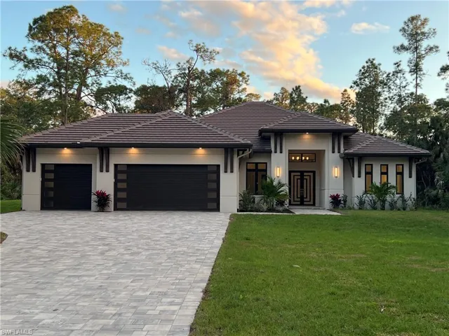 Prairie-style house featuring an attached garage, a lawn, decorative driveway, a tile roof, and stucco siding