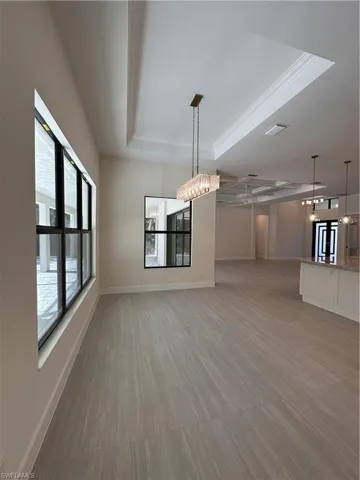 Unfurnished dining area featuring a chandelier, a raised ceiling, light wood-style flooring, and crown molding