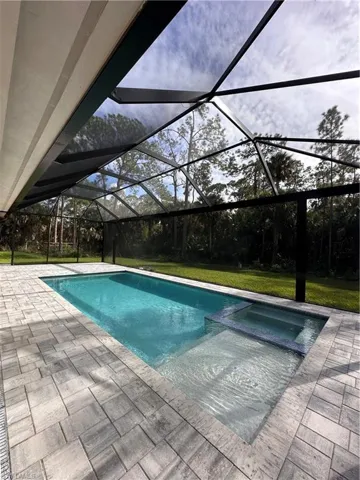 View of swimming pool featuring a sunroom, glass enclosure, a pool with connected hot tub, a patio, and a lawn