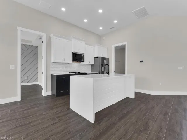 Two tone kitchen featuring electric stove, dual tone cabinetry, vaulted ceiling, light stone counters, and stainless steel microwave