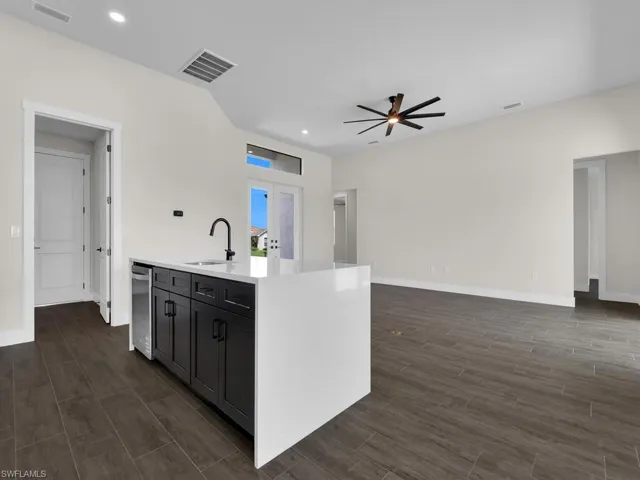 Kitchen with wood finish floors, light stone countertops, a center island with sink, hanging lights, and a glass covered fireplace