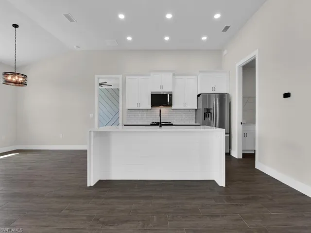 Kitchen with white cabinetry, stainless steel appliances, an island with sink, light stone counters, and backsplash