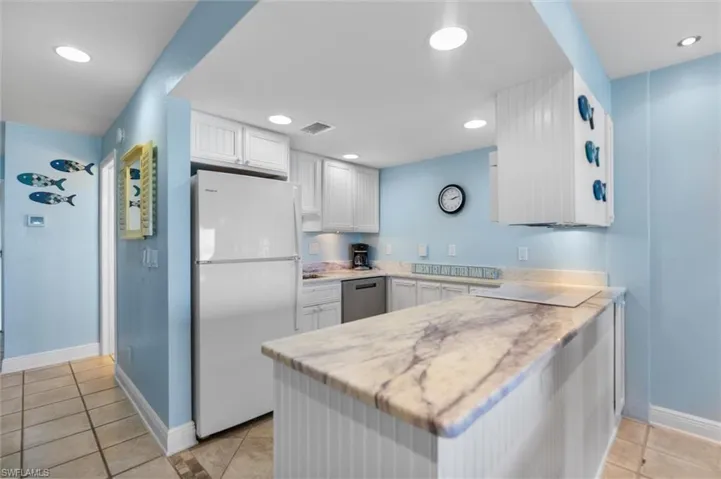 Kitchen with freestanding refrigerator, light tile patterned floors, a peninsula, white cabinets, and dishwasher