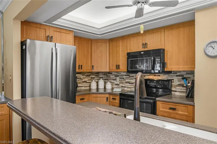 Kitchen featuring black appliances, dark countertops, ceiling fan, decorative backsplash, and brown cabinetry
