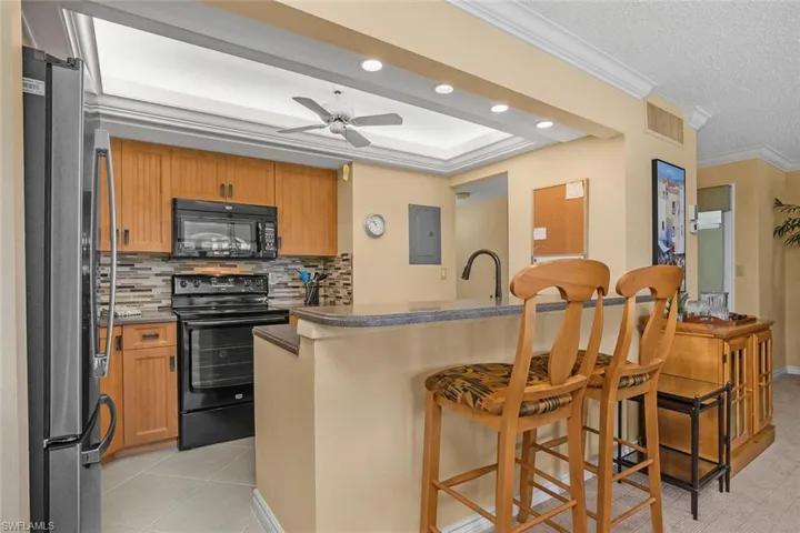 Kitchen featuring black appliances, electric panel, a breakfast bar, a ceiling fan, and decorative backsplash