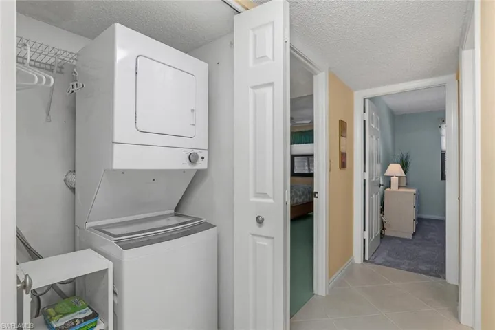 Washroom featuring stacked washer / dryer, a textured ceiling, light tile patterned flooring, and light colored carpet