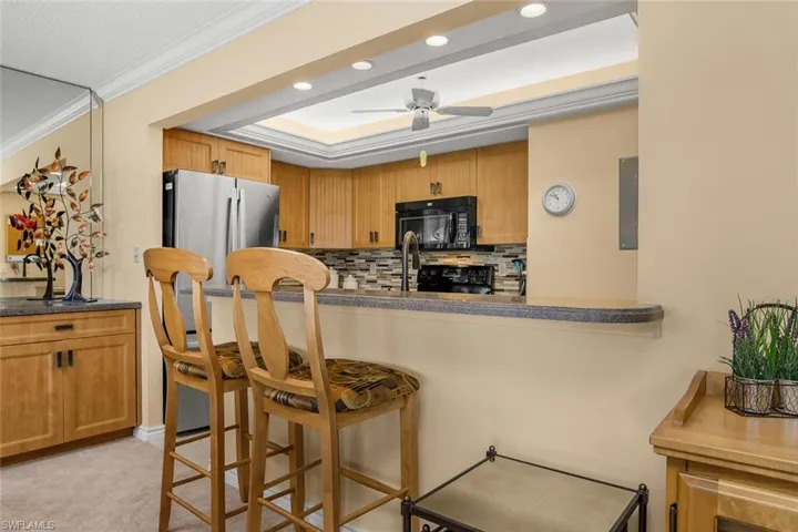 Kitchen featuring black microwave, a breakfast bar area, tasteful backsplash, ceiling fan, and dark countertops