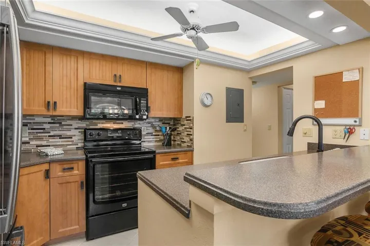 Kitchen with black appliances, dark countertops, electric panel, a peninsula, and backsplash