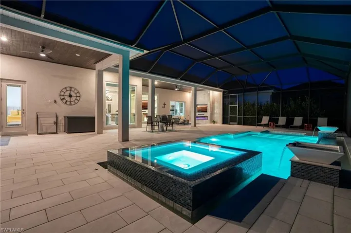 Pool at night featuring a ceiling fan, a patio area, a pool with connected hot tub, a sunroom, and glass enclosure