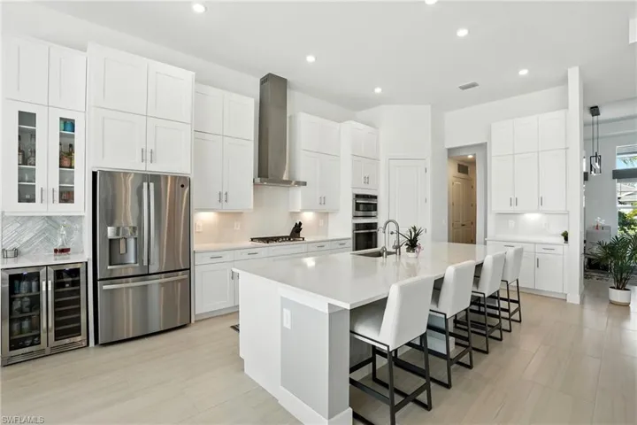 Kitchen with tasteful backsplash, beverage cooler, stainless steel appliances, a kitchen breakfast bar, and an island with sink