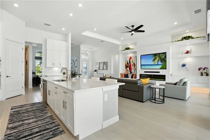 Kitchen with open floor plan, white cabinetry, light stone counters, a center island with sink, and recessed lighting