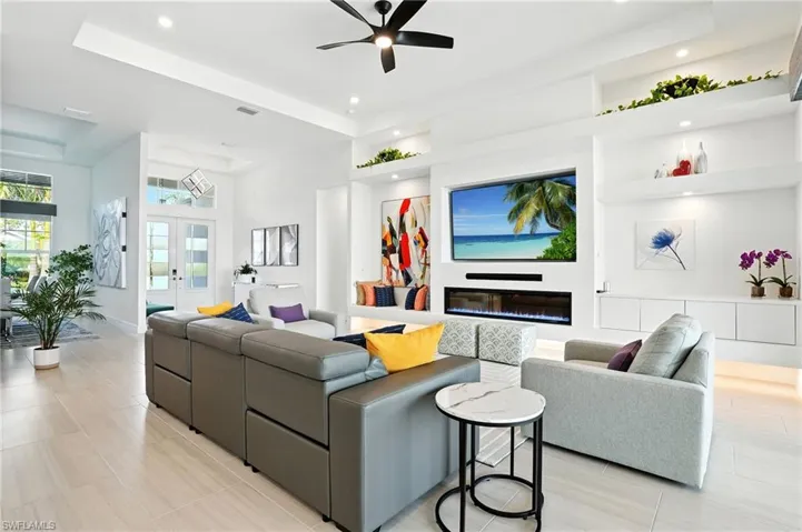 Living room featuring french doors, a glass covered fireplace, a ceiling fan, recessed lighting, and a high ceiling