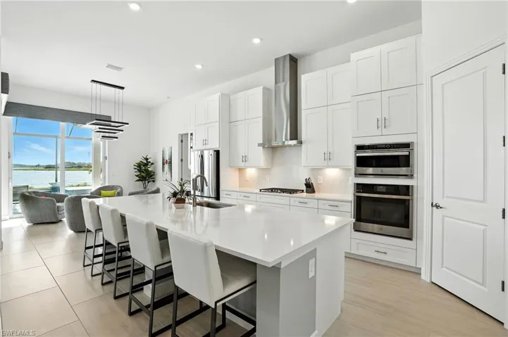 Kitchen featuring a kitchen breakfast bar, white cabinets, a kitchen island with sink, wall chimney range hood, and hanging light fixtures