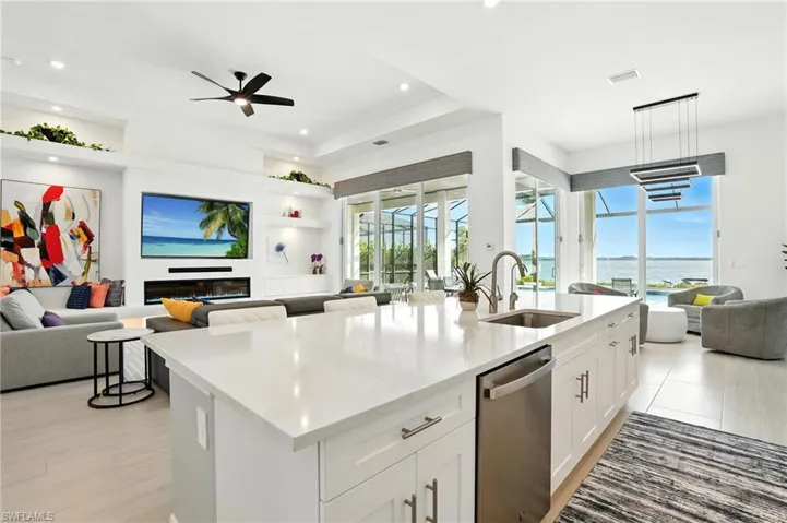 Kitchen featuring open floor plan, light stone counters, white cabinets, a kitchen island with sink, and stainless steel dishwasher