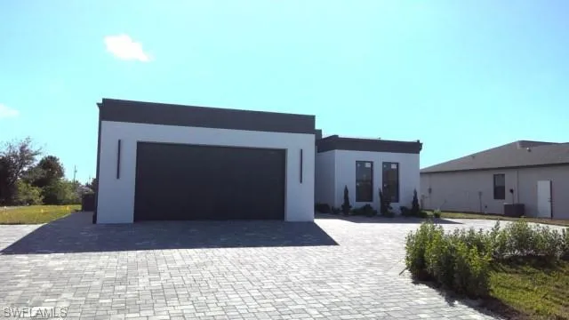 Modern architecture featuring a grey and white stucco exterior, dark garage door, and a paver driveway