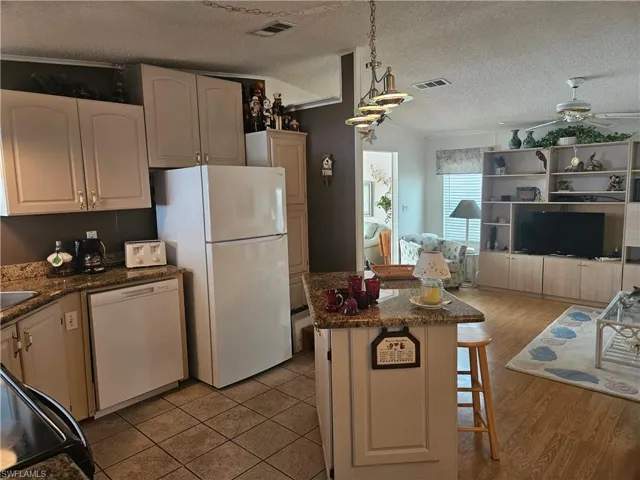 Kitchen with a textured ceiling, ceiling fan, white appliances, and visible vents