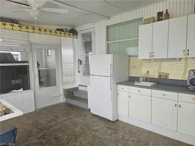 Kitchen with freestanding refrigerator, a sink, a ceiling fan, and dark countertops