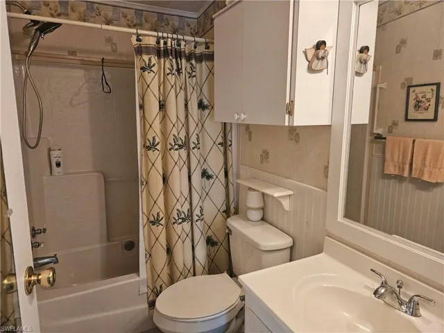 Bathroom featuring toilet, shower / bathtub combination with curtain, vanity, and wallpapered walls