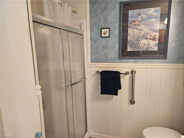 Bathroom with toilet, a stall shower, and wainscoting
