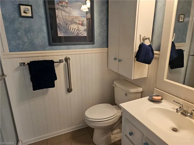 Bathroom featuring toilet, tile patterned floors, a wainscoted wall, and vanity