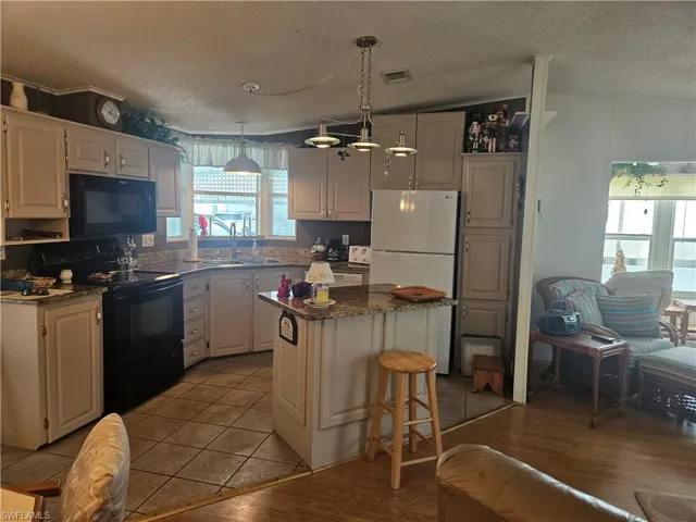 Kitchen featuring a textured ceiling, visible vents, black appliances, a center island, and a sink