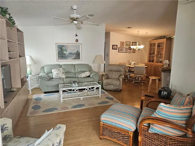 Living room with ceiling fan with notable chandelier, a textured ceiling, and wood finished floors