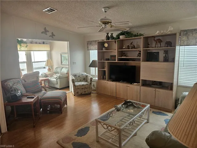 Living area with visible vents, a ceiling fan, a textured ceiling, light wood finished floors, and vaulted ceiling