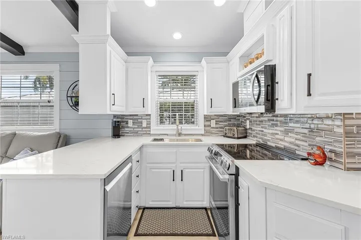 Kitchen featuring stainless steel appliances, white cabinetry, light stone counters, ornamental molding, and a peninsula