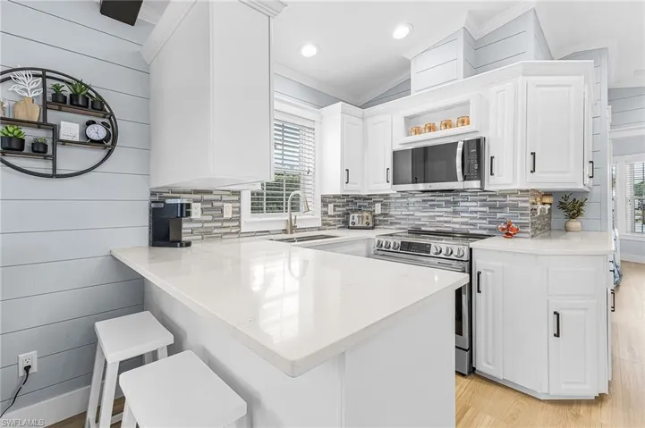 Kitchen featuring a breakfast bar, stainless steel appliances, a peninsula, light wood-type flooring, and crown molding