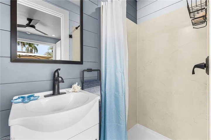 Full bathroom with a shower stall, vanity, a ceiling fan, and wood walls