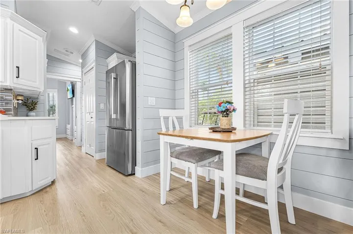 Dining space featuring light wood finished floors, ornamental molding, hanging lights, and wooden walls