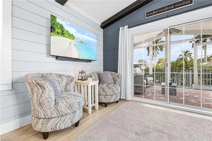 Living area with lofted ceiling, wooden walls, light wood-style floors, and ornamental molding