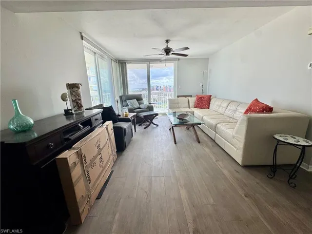 Living room with light wood-style flooring, a ceiling fan, and a wall of windows