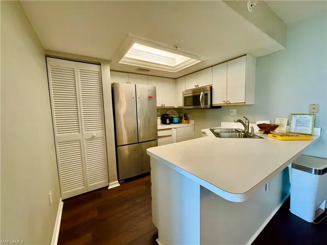 Kitchen featuring appliances with stainless steel finishes, a sink, a peninsula, dark wood-style flooring, and white cabinets