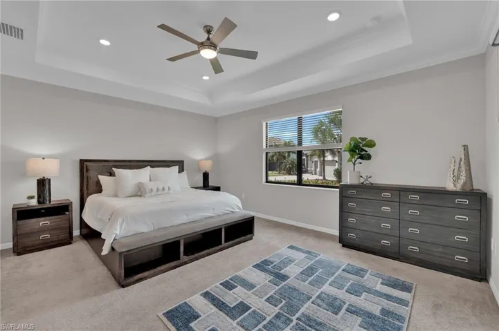 Bedroom with a tray ceiling, light carpet, crown molding, a ceiling fan, and recessed lighting