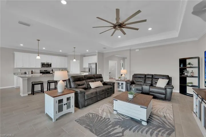 Living room with ornamental molding, arched walkways, recessed lighting, a tray ceiling, and a ceiling fan