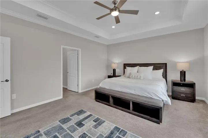 Bedroom featuring a raised ceiling, light colored carpet, a ceiling fan, ornamental molding, and recessed lighting