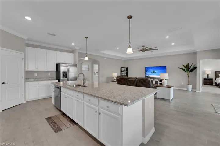 Kitchen with pendant lighting, white cabinets, arched walkways, light stone counters, and appliances with stainless steel finishes