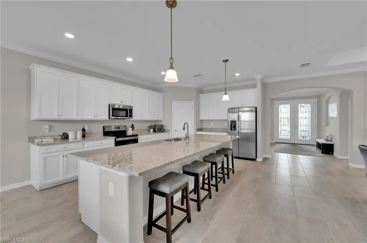 Kitchen with arched walkways, stainless steel appliances, a breakfast bar, white cabinetry, and crown molding