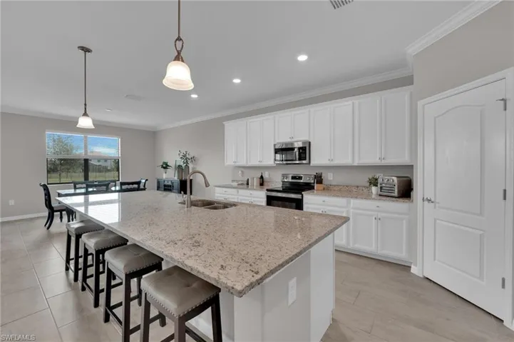 Kitchen featuring a kitchen bar, light stone countertops, white cabinets, decorative light fixtures, and stainless steel appliances