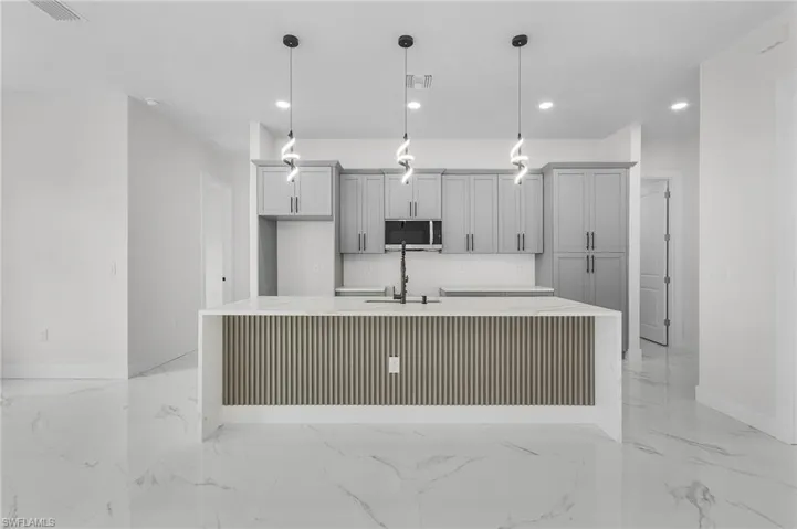 Kitchen featuring light tile patterned flooring, gray cabinetry, hanging light fixtures, and an island with sink
