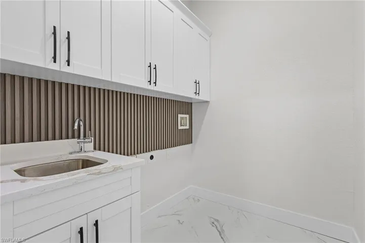 Laundry area featuring sink, electric dryer hookup, light tile patterned floors, and cabinets