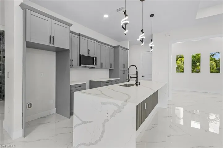 Kitchen featuring gray cabinetry, a kitchen island with sink, light tile patterned flooring, and light stone countertops