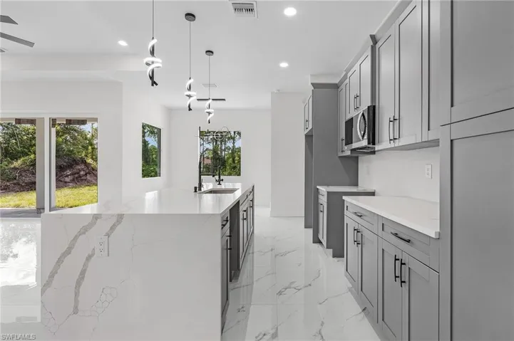 Kitchen with light stone countertops, a kitchen island with sink, light tile patterned floors, gray cabinets, and pendant lighting
