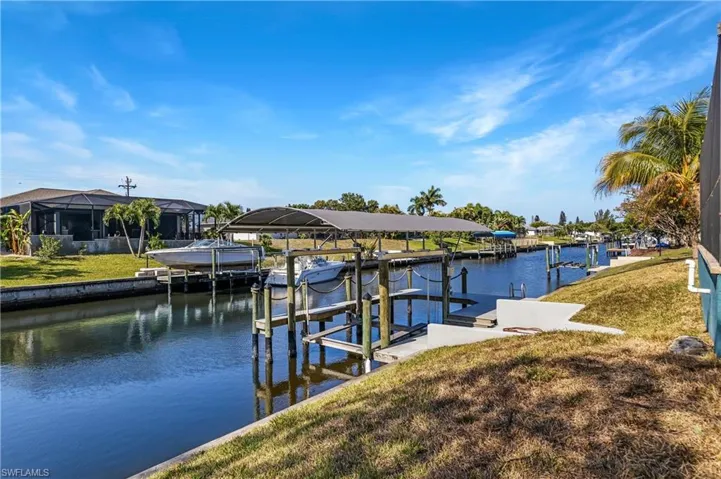 Dock with boat lift, a lawn, and a water view