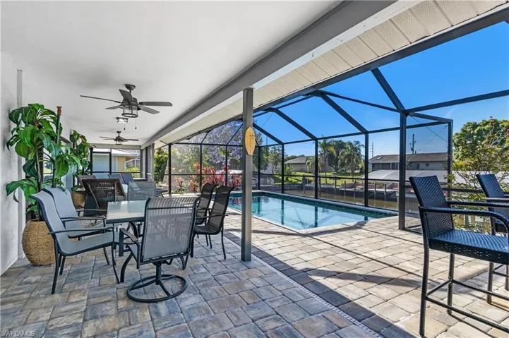 View of patio with outdoor dining area, a lanai, a sunroom, a ceiling fan, and an outdoor pool