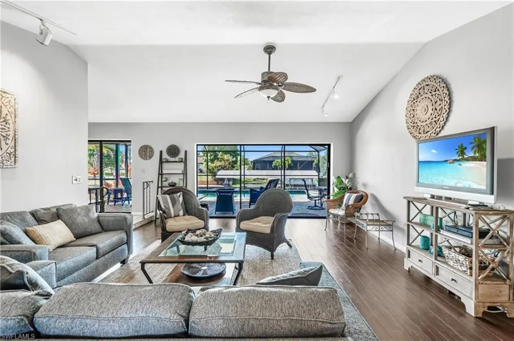 Living room with track lighting, a sunroom, vaulted ceiling, ceiling fan, and dark wood-type flooring