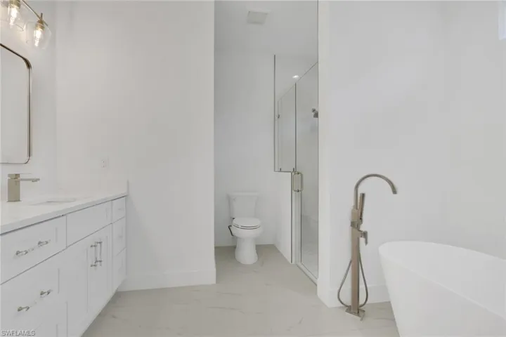Primary bathroom featuring vanity, a shower, a freestanding tub, and light marble finish floors